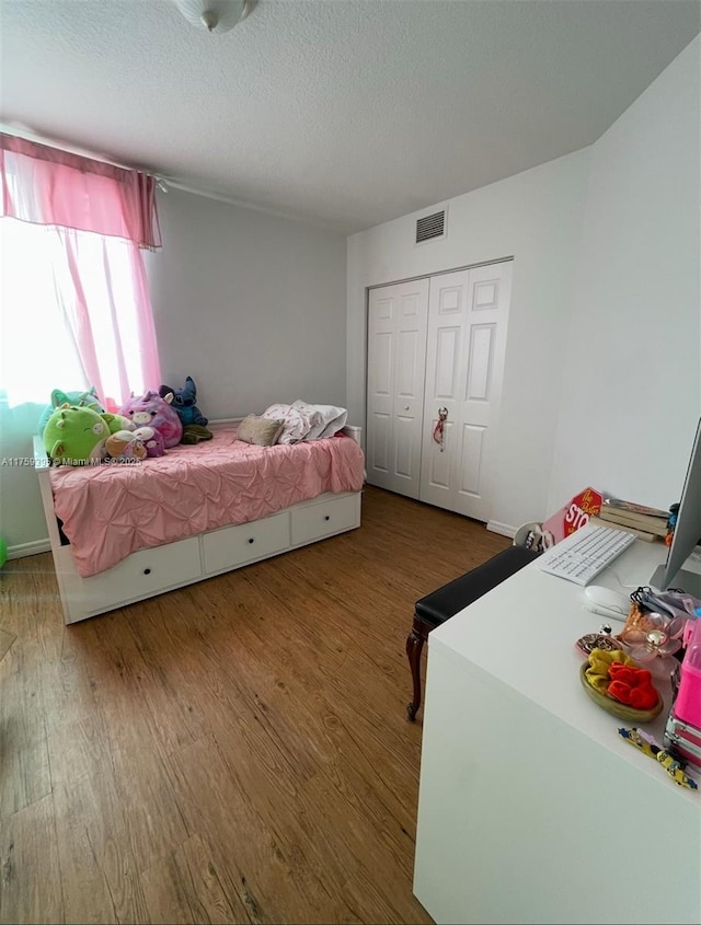 bedroom with a closet, visible vents, a textured ceiling, and wood finished floors