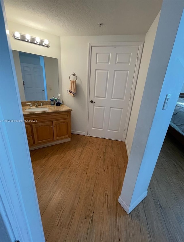 bathroom with a textured ceiling, baseboards, wood finished floors, and vanity