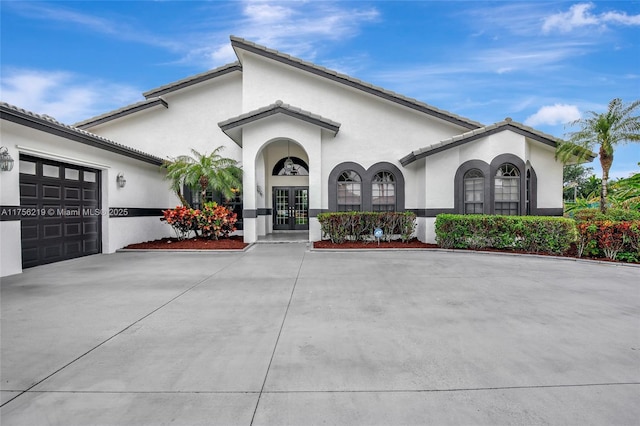 view of front of house featuring french doors, stucco siding, an attached garage, and driveway