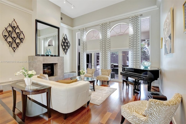 living area featuring a fireplace, wood finished floors, a towering ceiling, french doors, and rail lighting