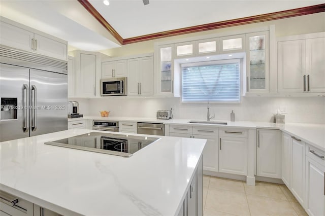 kitchen featuring built in appliances, a sink, vaulted ceiling, white cabinetry, and light countertops