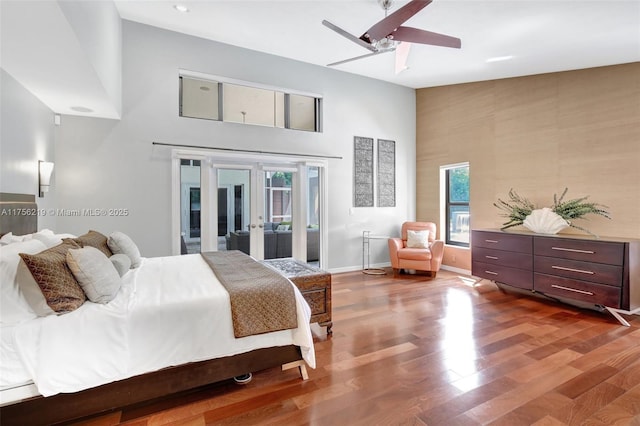 bedroom featuring french doors, access to outside, a towering ceiling, wood finished floors, and baseboards