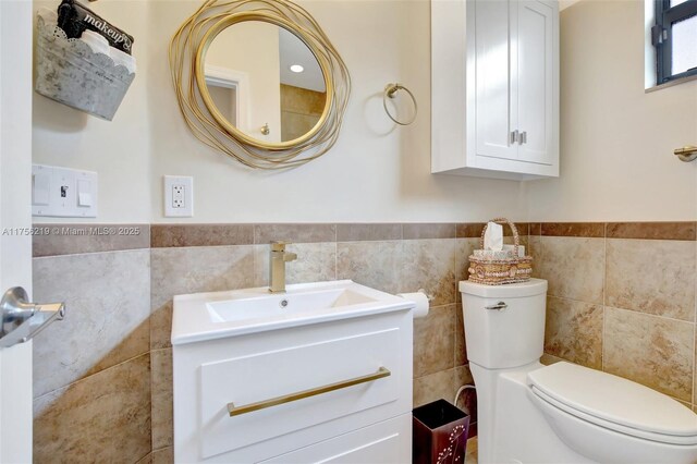 bathroom with tile walls, toilet, wainscoting, and vanity
