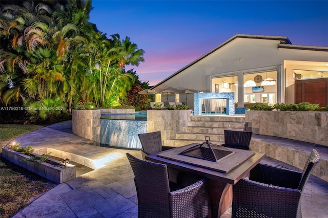 patio terrace at dusk with a swimming pool and a fire pit