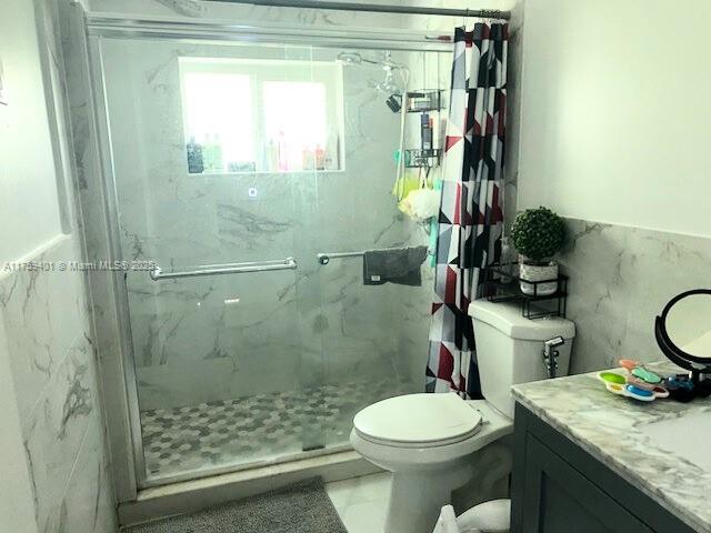 full bathroom with a wainscoted wall, tile walls, a marble finish shower, toilet, and vanity