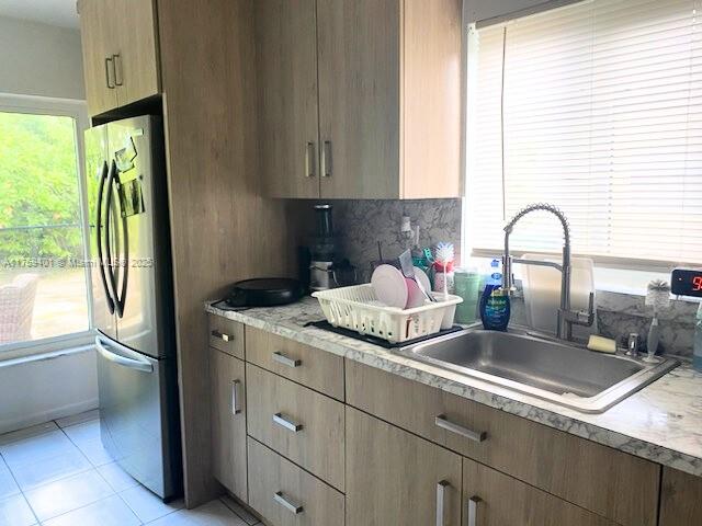 kitchen featuring light tile patterned floors, a sink, light countertops, freestanding refrigerator, and tasteful backsplash