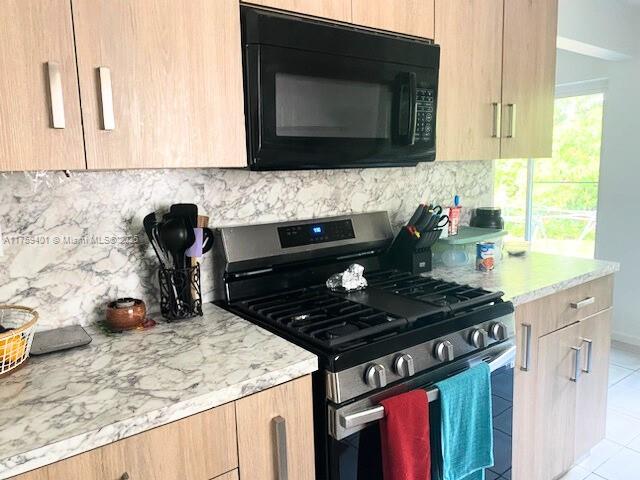 kitchen featuring light brown cabinets, black microwave, and gas stove