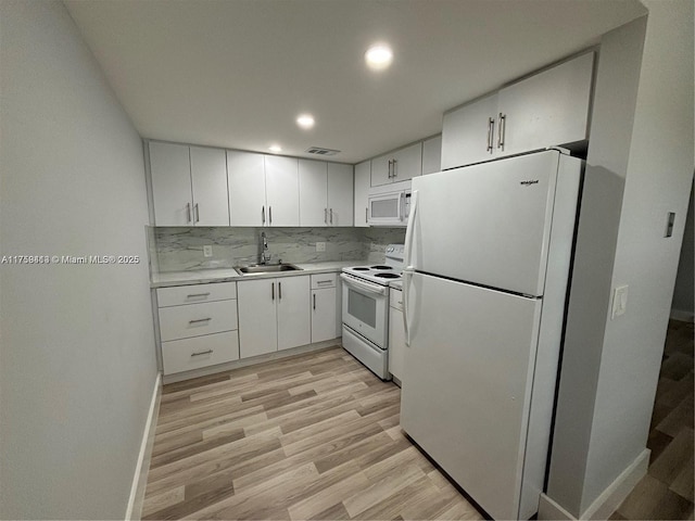 kitchen with white appliances, decorative backsplash, light countertops, light wood-style floors, and a sink