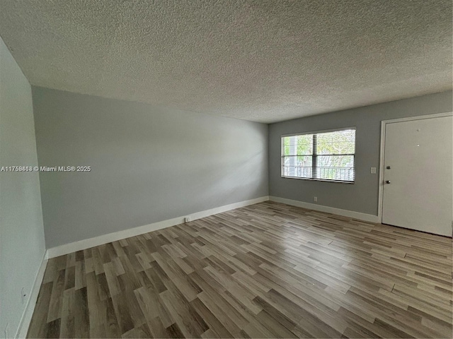 spare room featuring a textured ceiling, wood finished floors, and baseboards