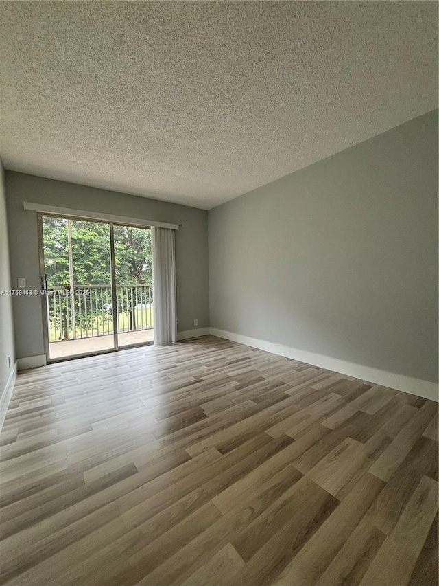 unfurnished room with a textured ceiling, baseboards, and wood finished floors