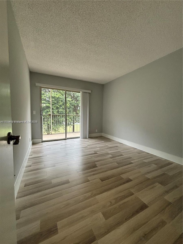 empty room with a textured ceiling, baseboards, and wood finished floors