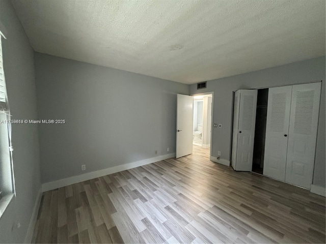 unfurnished bedroom featuring a closet, visible vents, a textured ceiling, wood finished floors, and baseboards