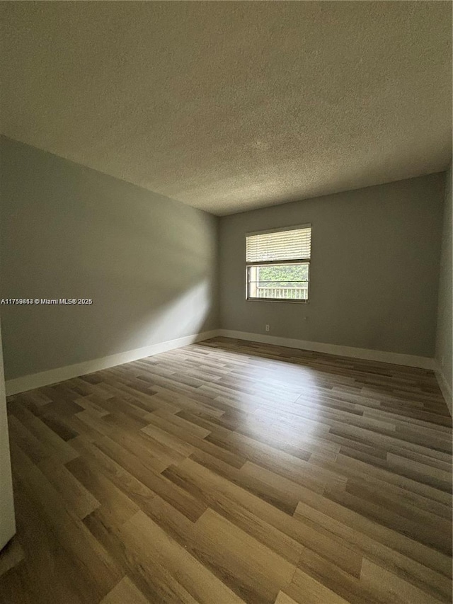 unfurnished room featuring a textured ceiling, wood finished floors, and baseboards