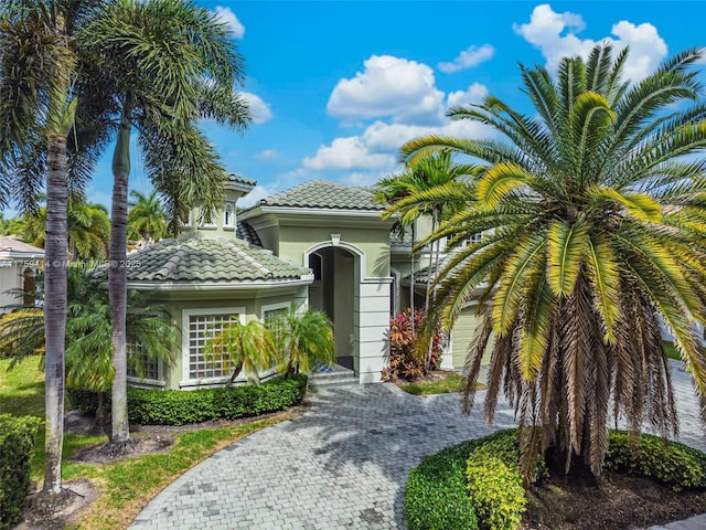 view of front facade featuring a garage, decorative driveway, a tiled roof, and stucco siding