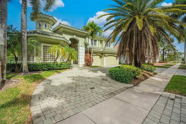 mediterranean / spanish-style house featuring a garage, a tile roof, decorative driveway, and stucco siding