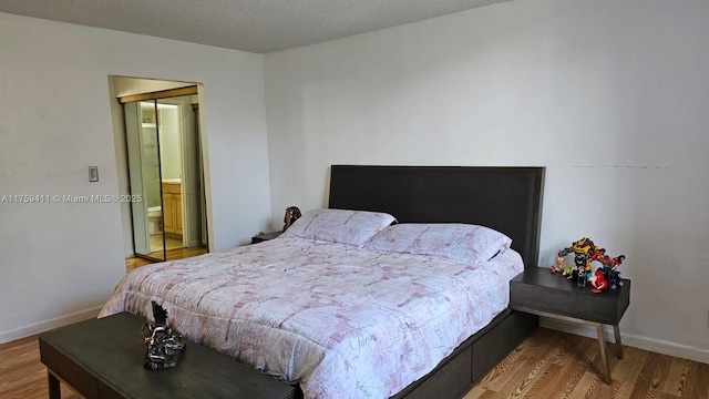 bedroom with a textured ceiling, baseboards, and wood finished floors