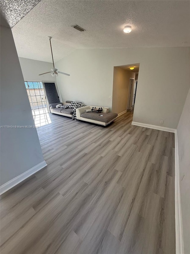 interior space with a textured ceiling, wood finished floors, visible vents, baseboards, and vaulted ceiling