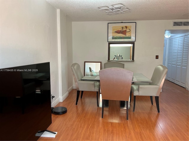 dining space featuring baseboards, a textured ceiling, visible vents, and wood finished floors