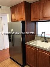 kitchen featuring light wood-style flooring, brown cabinets, a sink, and black fridge with ice dispenser