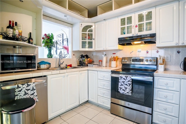 kitchen featuring under cabinet range hood, tile counters, appliances with stainless steel finishes, and a sink