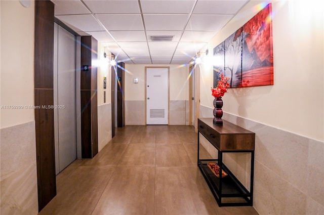 hall featuring a paneled ceiling, elevator, and visible vents