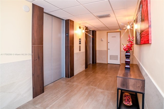 hall with visible vents, a paneled ceiling, and elevator