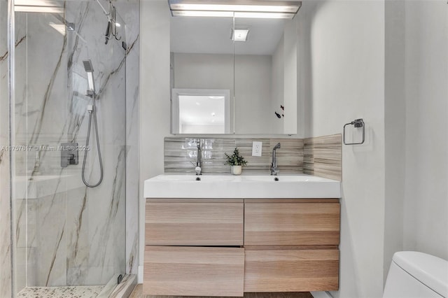 full bath with toilet, double vanity, a sink, and a marble finish shower