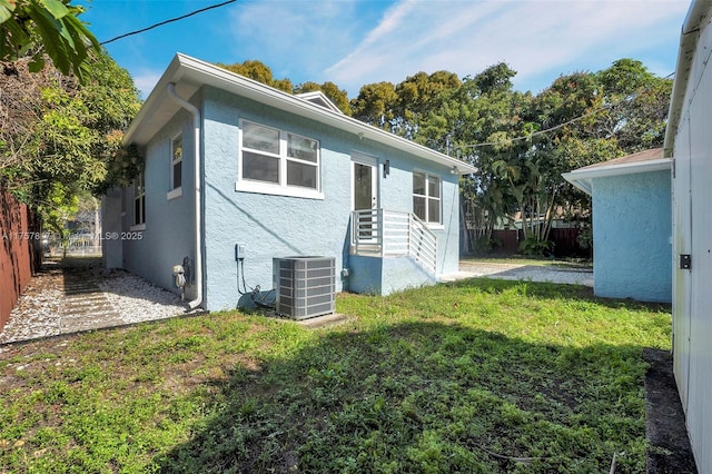 back of property with a yard, fence, cooling unit, and stucco siding