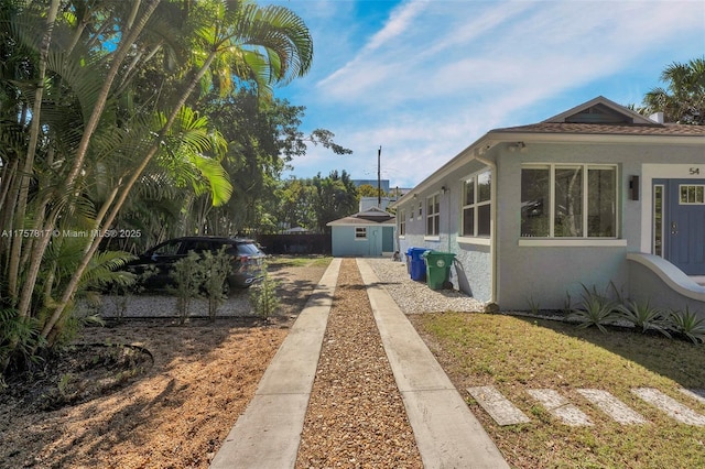 view of side of home with a storage shed, an outdoor structure, and stucco siding