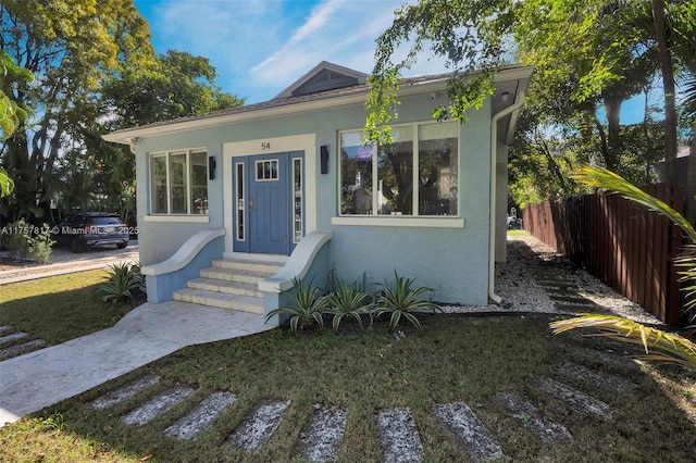 bungalow-style home with entry steps, fence, and stucco siding