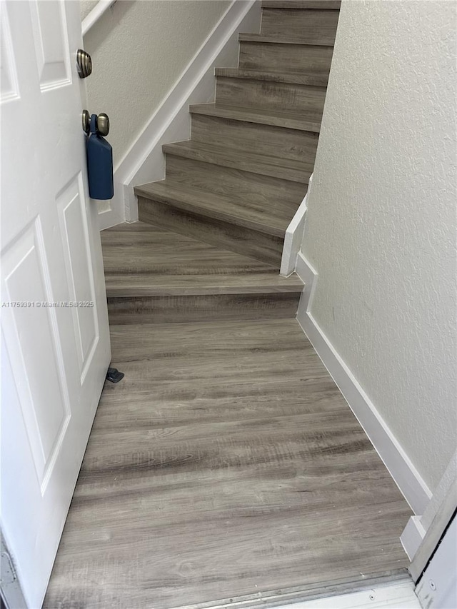 staircase featuring wood finished floors, a textured wall, and baseboards