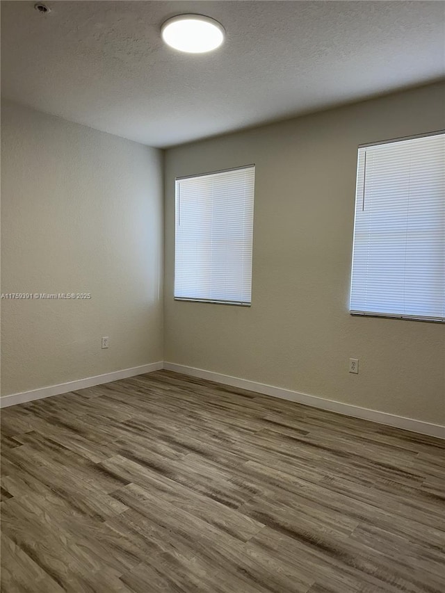 empty room featuring wood finished floors, baseboards, and a textured ceiling