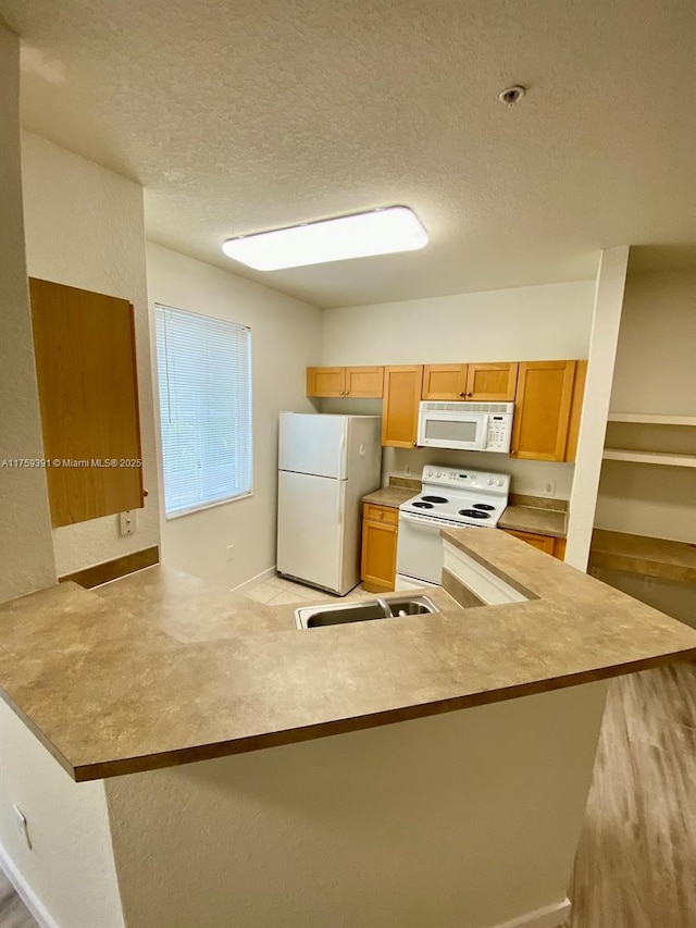 kitchen featuring a sink, a textured ceiling, white appliances, a peninsula, and light countertops