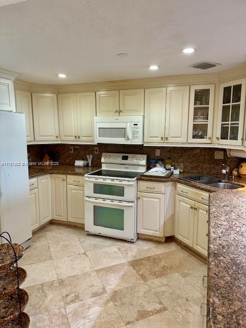 kitchen featuring visible vents, backsplash, glass insert cabinets, a sink, and white appliances