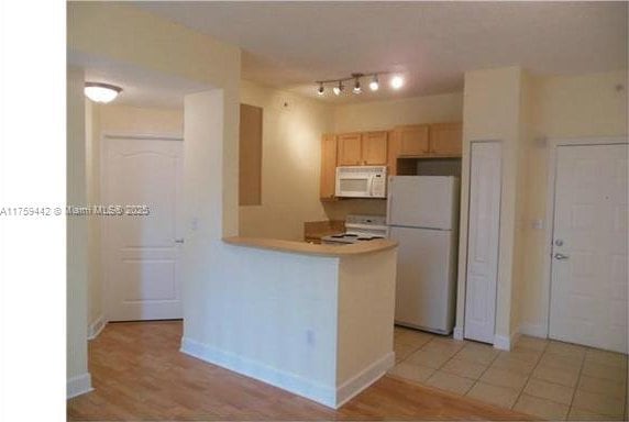 kitchen with a peninsula, white appliances, baseboards, light countertops, and light brown cabinetry