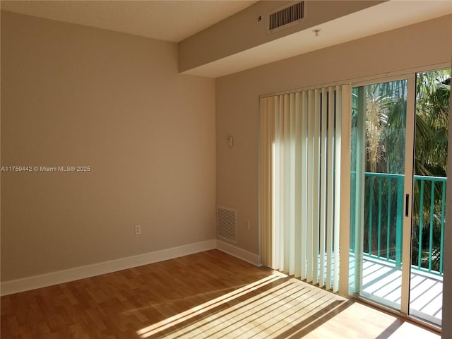 empty room featuring wood finished floors, visible vents, and baseboards