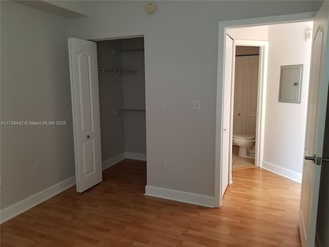 unfurnished bedroom featuring baseboards, light wood-style floors, a closet, electric panel, and a walk in closet