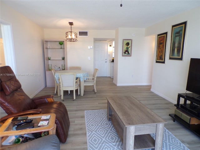 living room with visible vents, a notable chandelier, light wood-style flooring, and baseboards