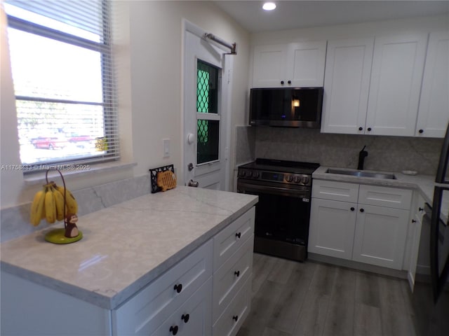 kitchen featuring range with electric cooktop, white cabinets, stainless steel microwave, light wood-type flooring, and a sink