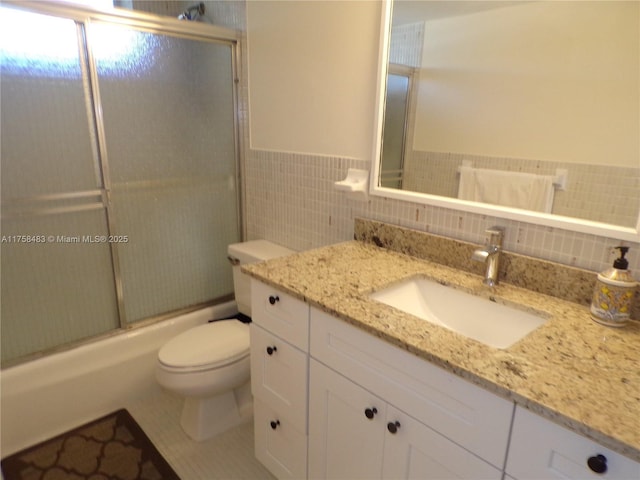 full bathroom with enclosed tub / shower combo, toilet, vanity, tile walls, and wainscoting