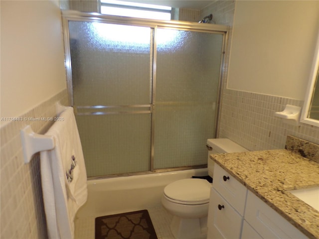 bathroom with wainscoting, toilet, enclosed tub / shower combo, vanity, and tile walls