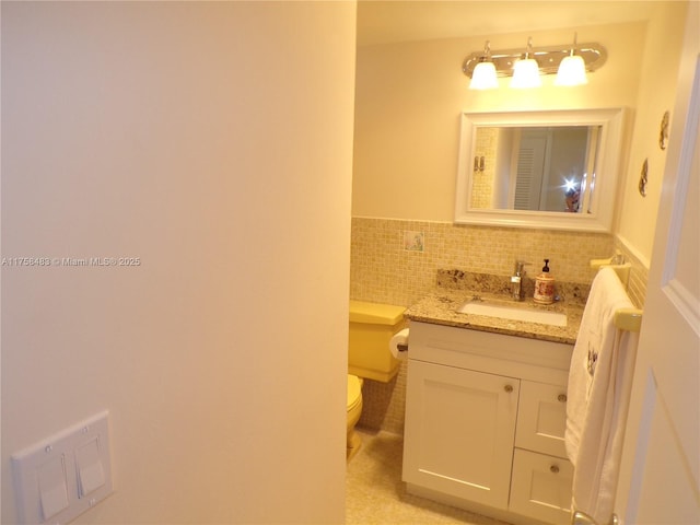 bathroom featuring toilet, wainscoting, tile walls, and vanity