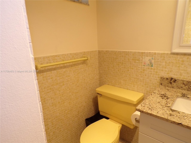 bathroom featuring toilet, a wainscoted wall, tile walls, and vanity