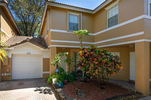 view of front of house featuring an attached garage, a tiled roof, decorative driveway, and stucco siding