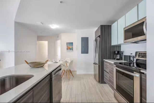 kitchen featuring stainless steel appliances, light countertops, a sink, electric panel, and baseboards