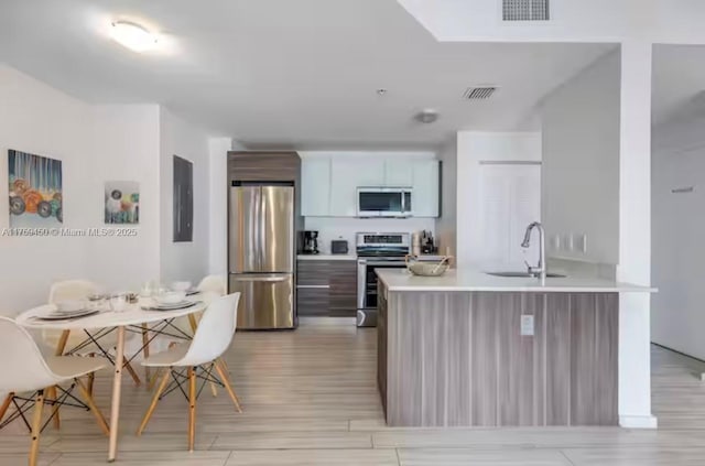 kitchen with a peninsula, a sink, visible vents, light countertops, and appliances with stainless steel finishes