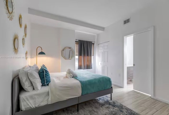 bedroom featuring ensuite bath, wood finished floors, visible vents, and baseboards