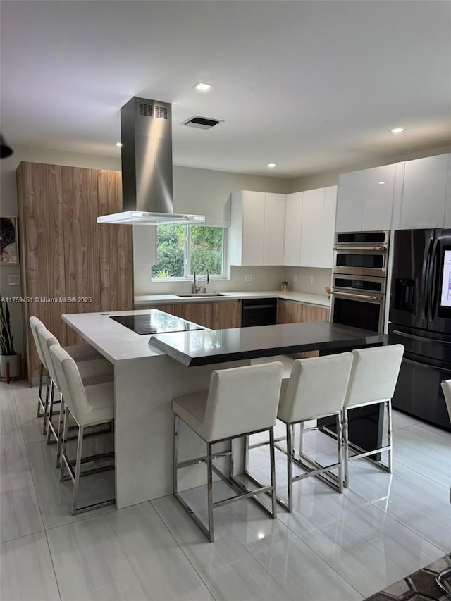 kitchen featuring black appliances, a kitchen bar, modern cabinets, and island range hood