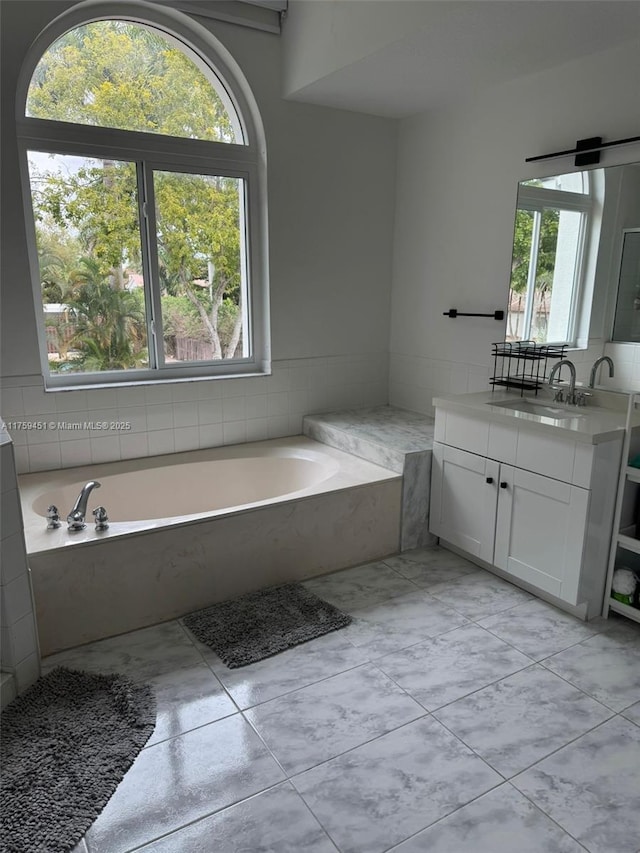 full bath featuring a healthy amount of sunlight, a garden tub, marble finish floor, and vanity