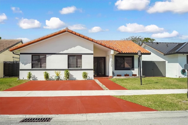 view of front of home with fence, a tiled roof, a front lawn, and stucco siding